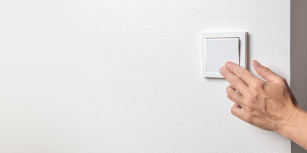 una mano de mujer apagando un interruptor de luz en una pared blanca scaled